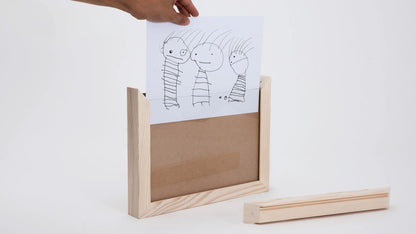 Kinderzeichnung wird in einen Bilderrahmen aus Tannenholz geschoben.